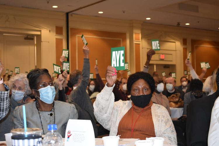 Diocesan Convention members raise "Aye" voting cards to create a Reparations Fund